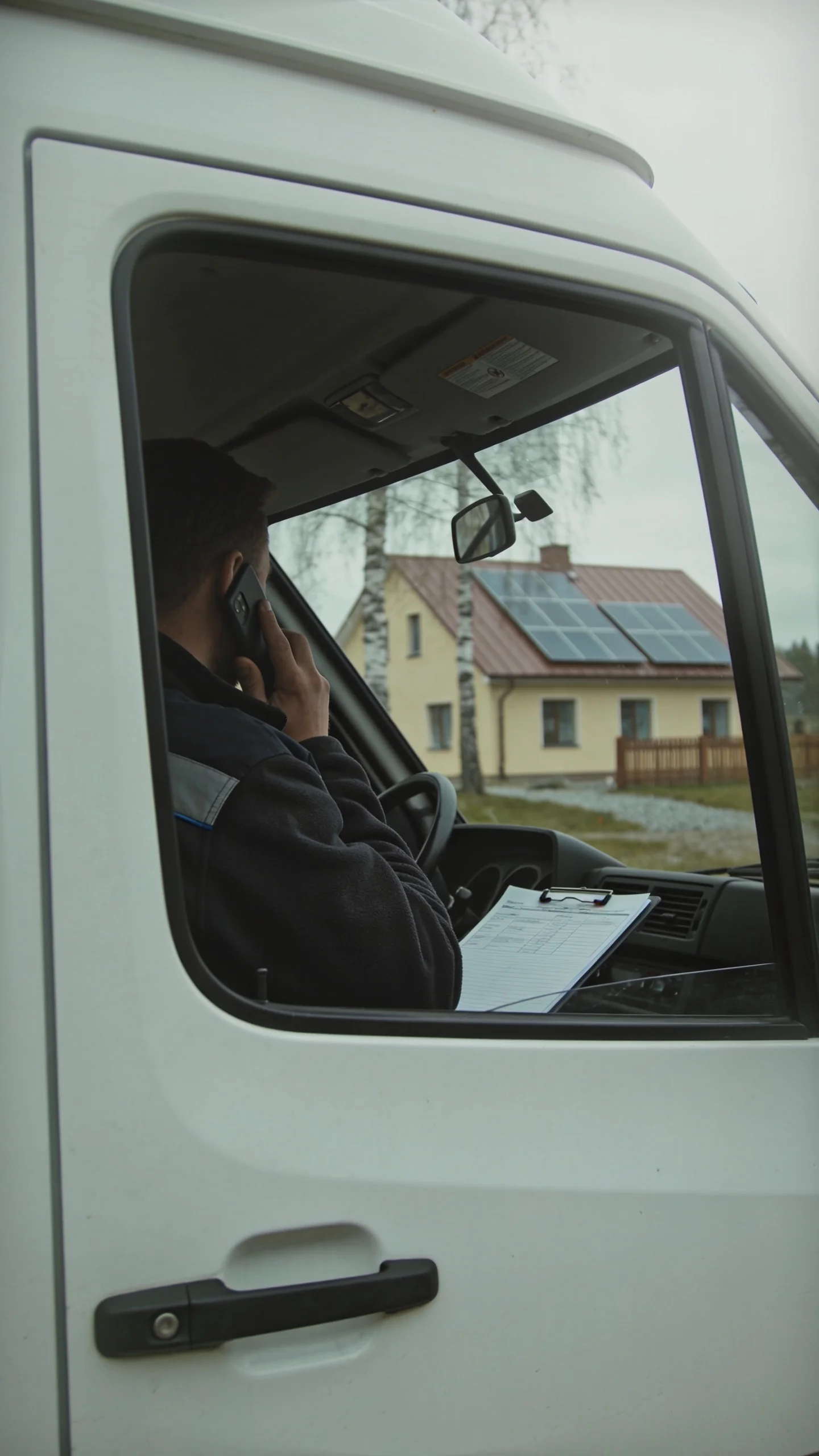 Montuotojas kalba telefonu furgone, už jo – namas su saulės elektrine